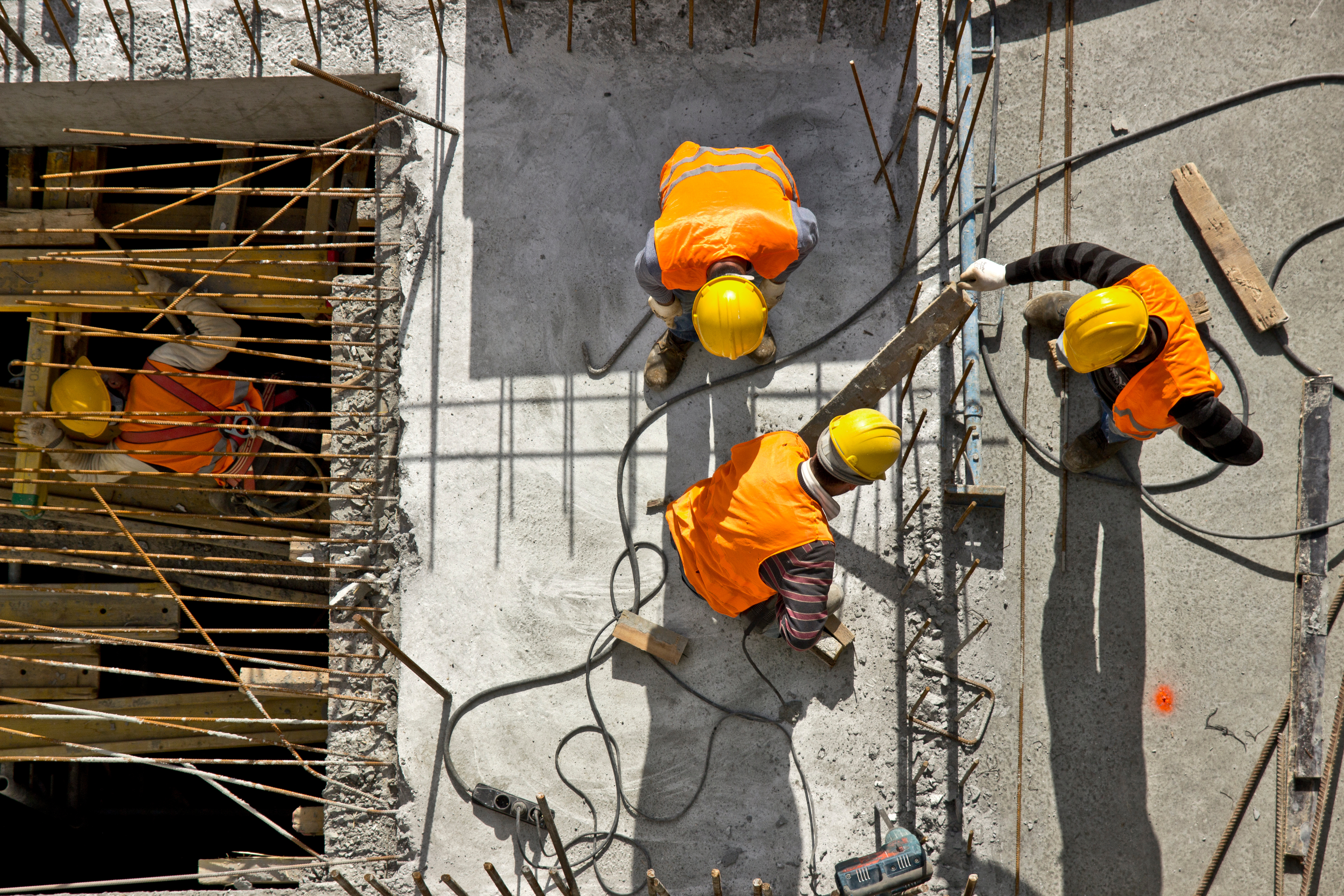 Construction workers wearing orange vests and yellow helmets working on a concrete structure, viewed from above