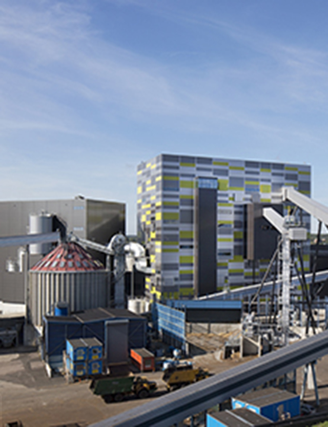 Industribyggnad med färgglad fasad, omgiven av industriella strukturer och utrustning, under en blå himmel.