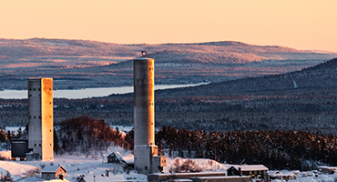 Två höga betongtorn omgivna av skog och snölandskap under en solnedgång.