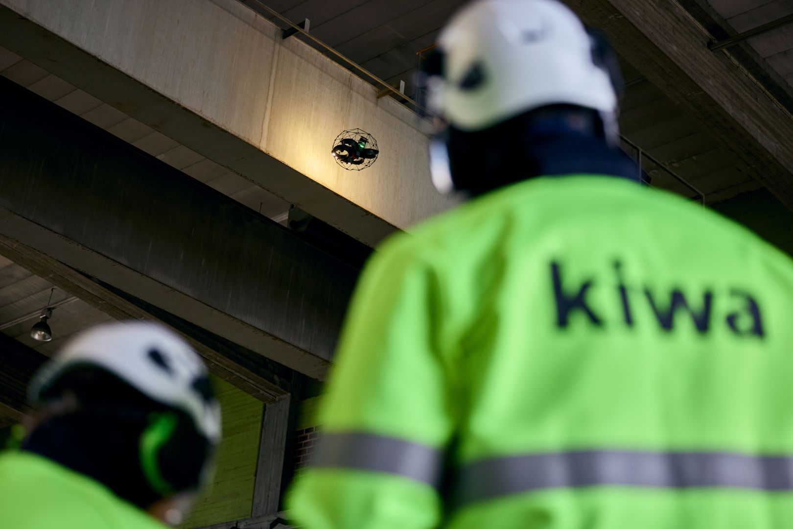 Kiwa employees in high-visibility jackets observe a drone inspecting industrial infrastructure indoors