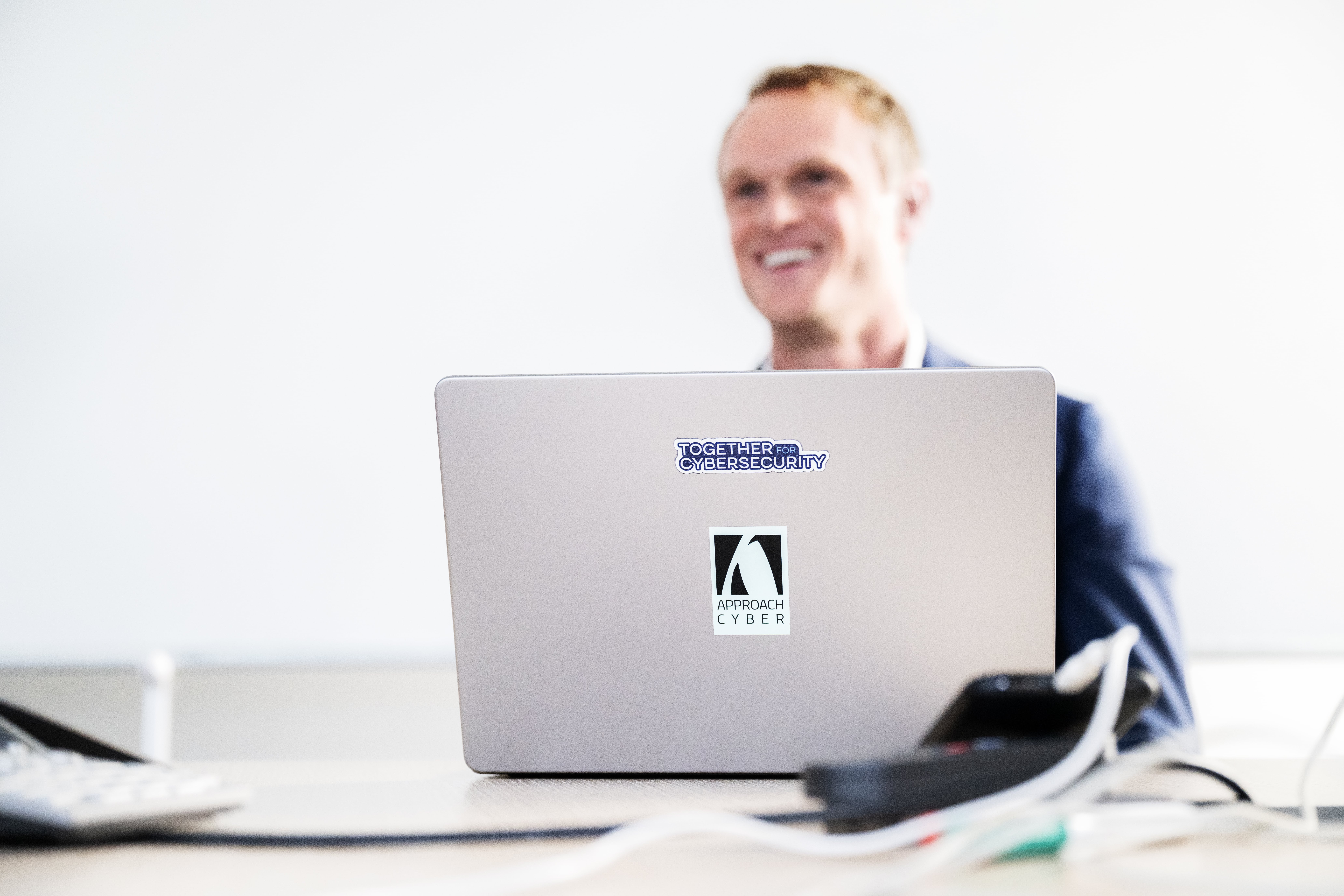 Smiling person working on a laptop with a "Together for Cybersecurity" sticker, emphasizing cybersecurity awareness