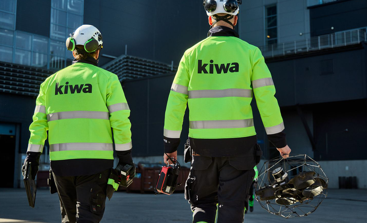 Kiwa auditors in fluorescent green Kiwa jackets carrying equipment outside an industrial building