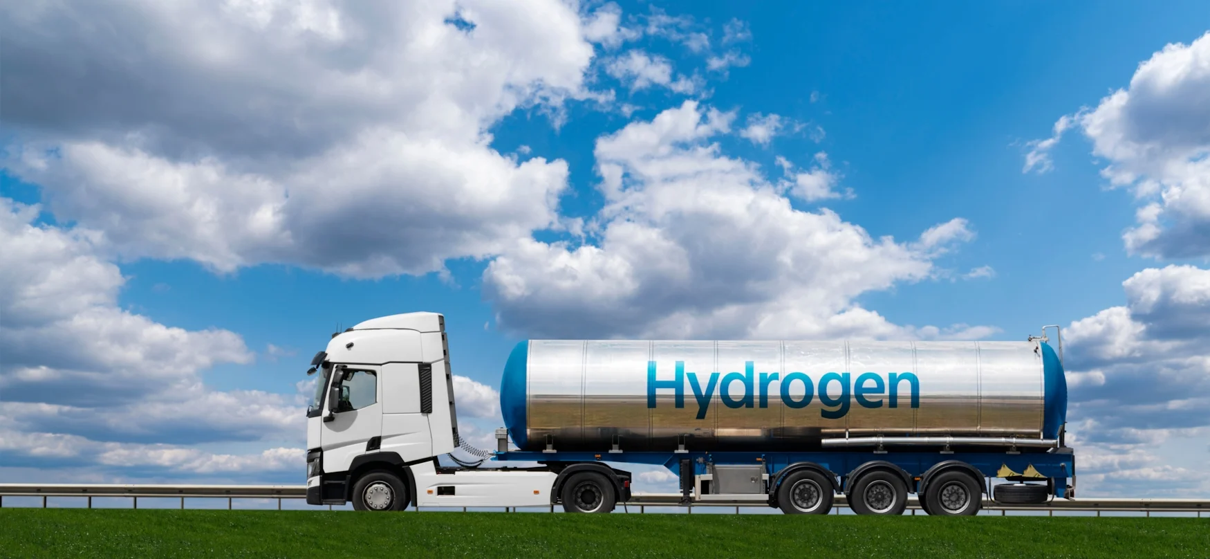 A white truck carrying a hydrogen tank trailer driving on a road with green grass under a blue sky with clouds.