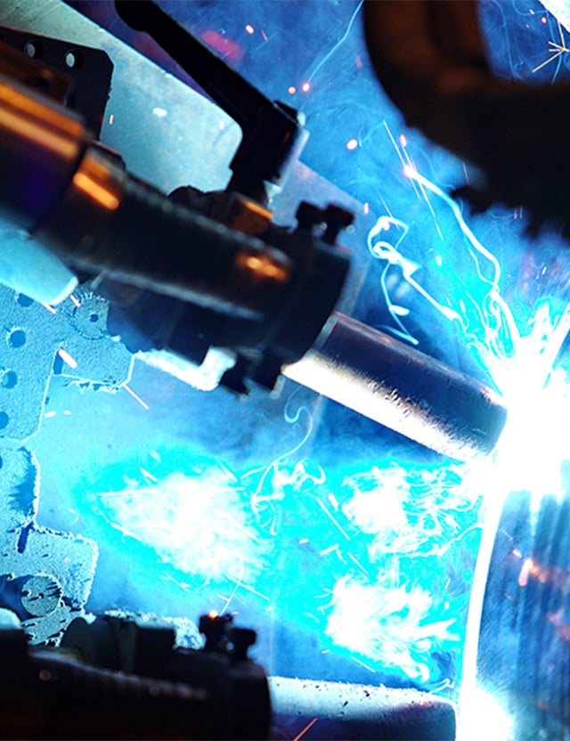 Svetsning med starkt blått ljus och gnistor, metallkomponenter synliga i bakgrunden.