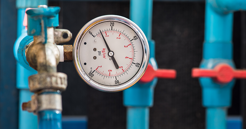 Manometer monterad på vattenrör med ventiler i blå och röda färger i bakgrunden.