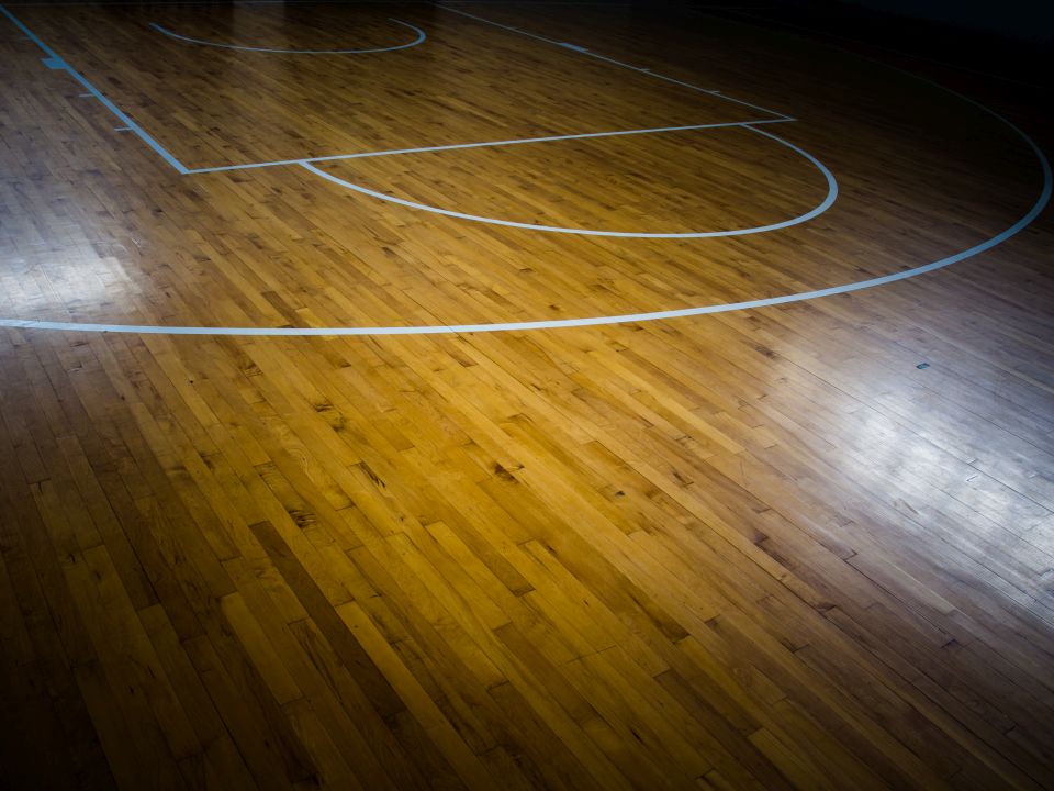 Basketbalveld met houten vloer en wit gemarkeerde lijnen.
