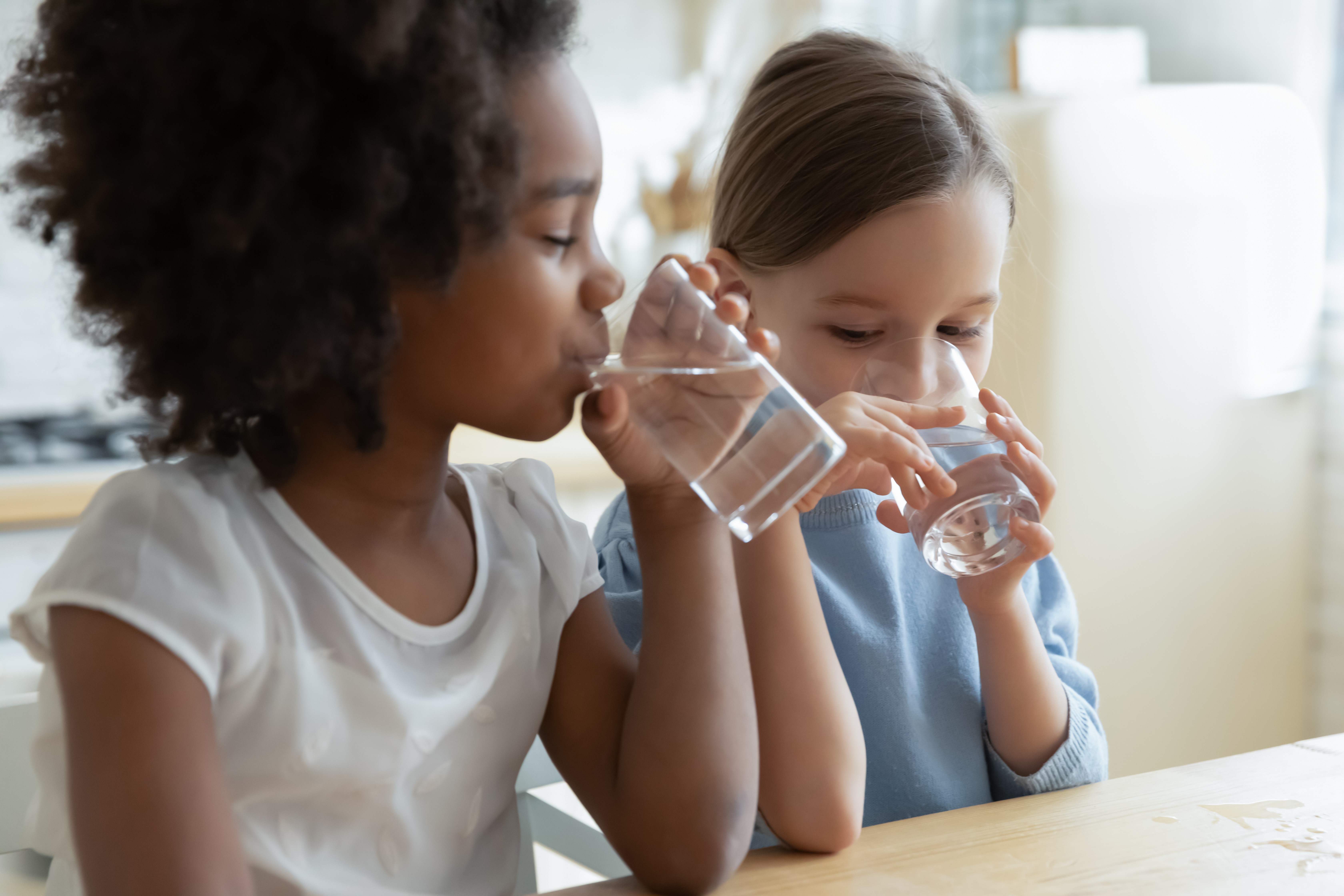 Deux enfants assis à une table, buvant de l'eau dans des verres.