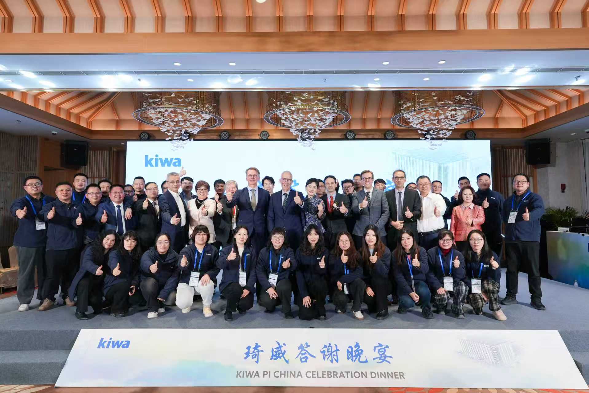 Group photo of Kiwa PI China Celebration Dinner attendees, posing and smiling with thumbs up in a decorated banquet hall