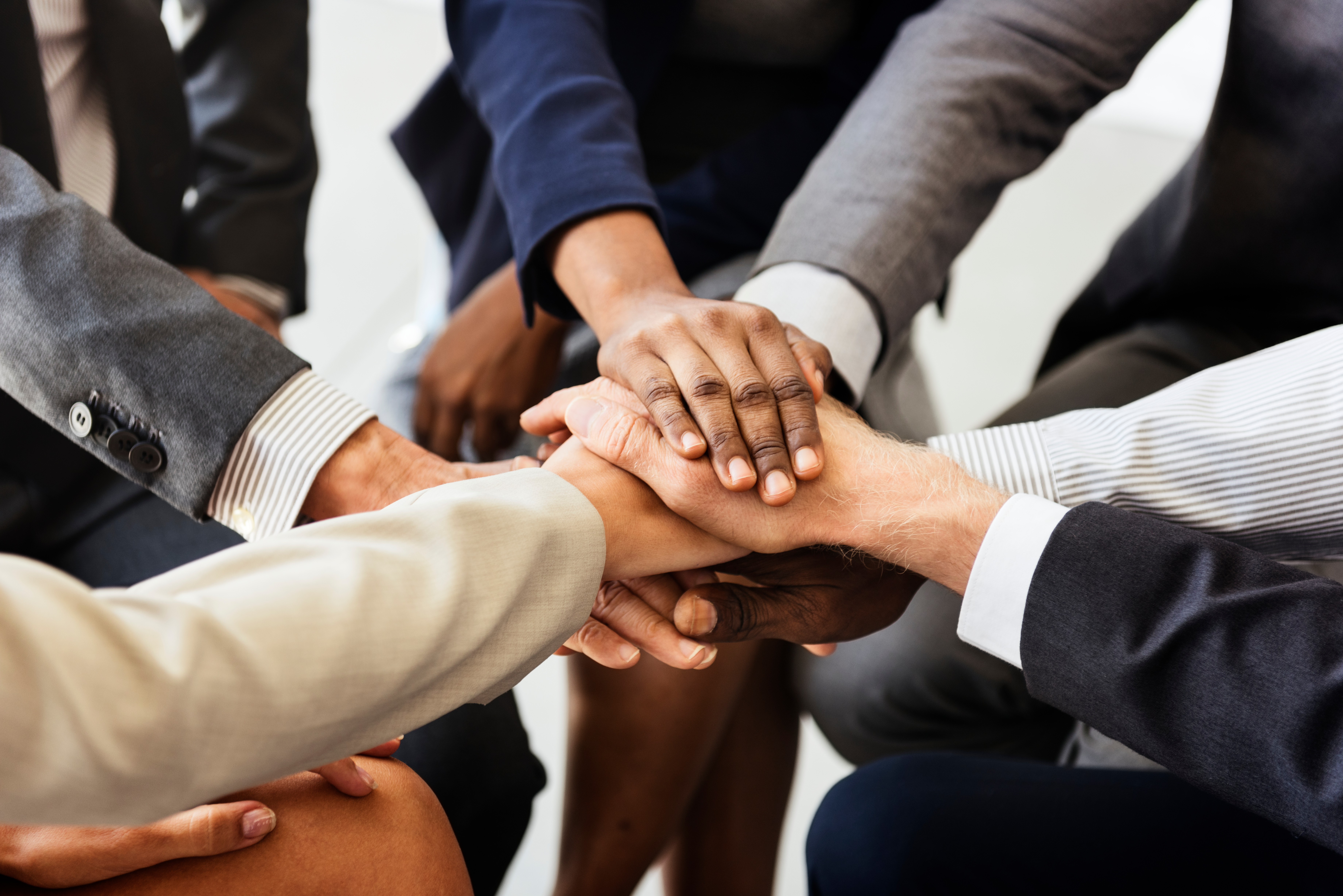 Diverse group of professionals placing hands together in teamwork gesture, symbolizing unity and collaboration