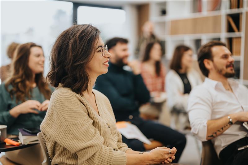 A diverse group of adults attentively listening during a seminar or workshop, seated in a modern classroom setting