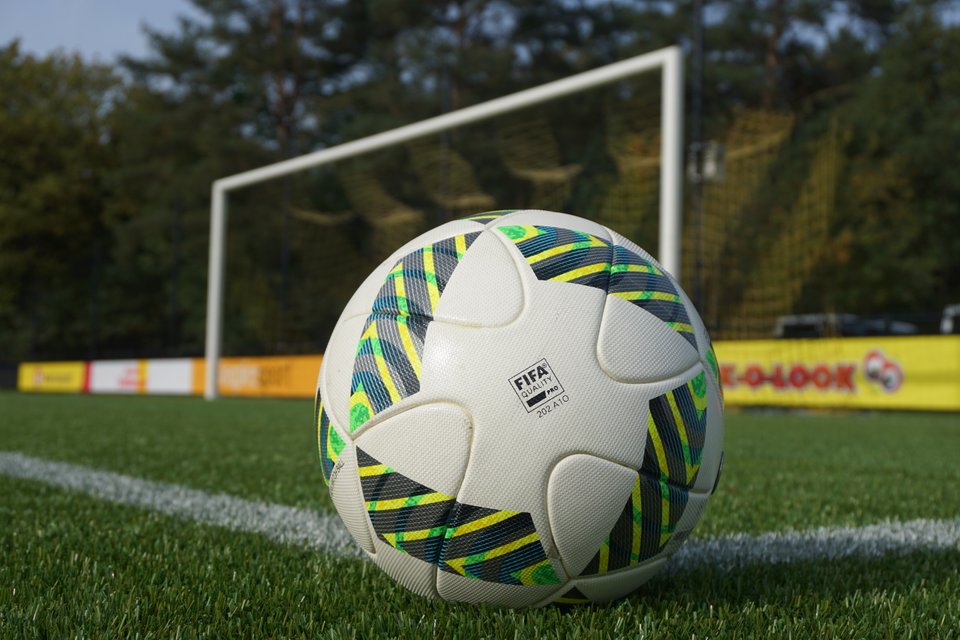 Close-up of a FIFA-approved soccer ball on a green field with a goalpost in the background