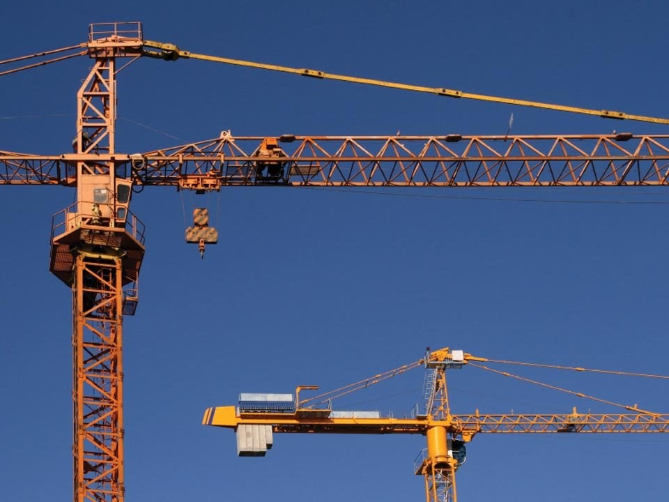 Two Kiwa inspected yellow construction cranes against a clear blue sky, showcasing industrial machinery used for building projects