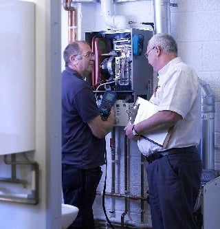 Two technicians inspecting and discussing a heating system in a utility room