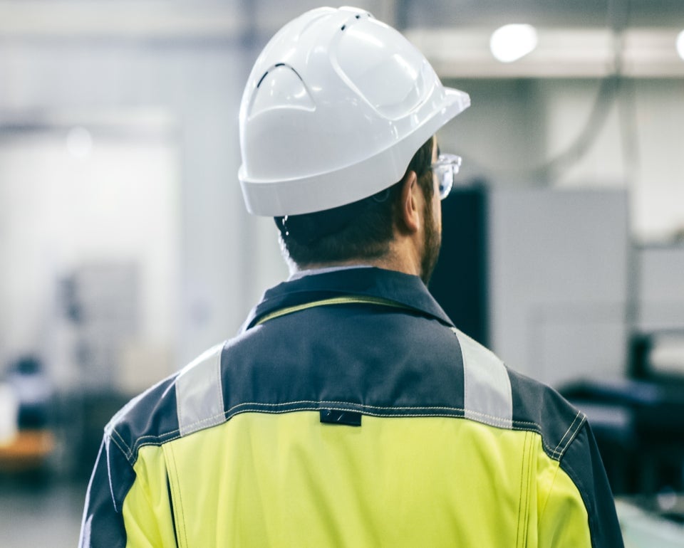 Hombre con casco de seguridad y chaqueta de alta visibilidad en un entorno industrial.