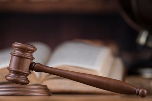 Houten hamer op een houten onderstel, met geopende boeken en een globe op de achtergrond.