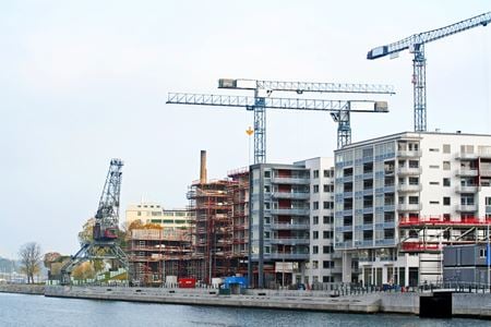 Woongebouwen in aanbouw bij een waterkant, met meerdere bouwkranen en steigers zichtbaar.
