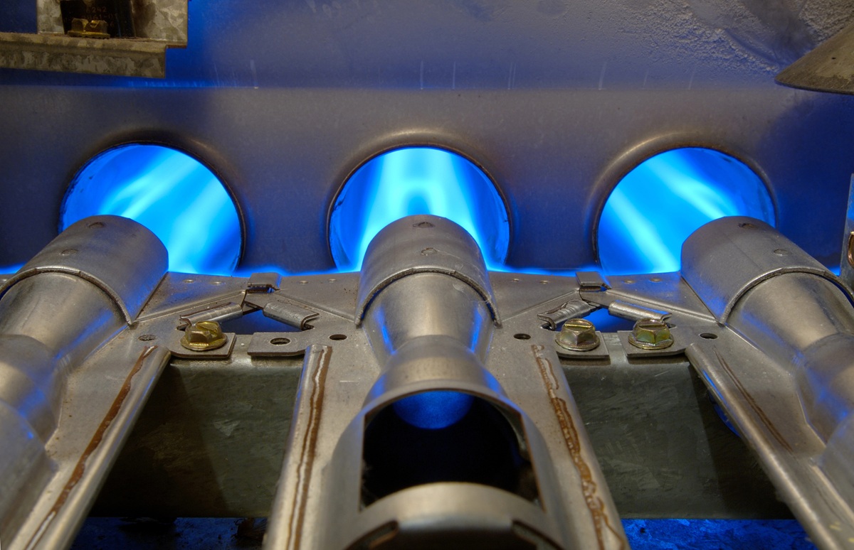 Close-up of a gas furnace with three blue flames burning inside metal tubes.