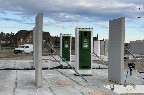 Bouwplaats met betonnen muren en fundamenten, omgeven door groene bouwcontainers