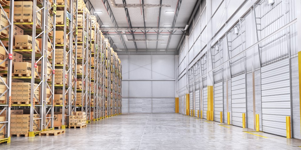 Opslagruimte met stellingen gevuld met dozen aan de linkerzijde en een lege vloer met gesloten roldeuren aan de rechterzijde.