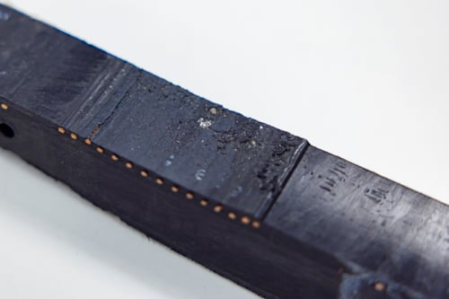 Zwart rechthoekig object met een matte afwerking, zichtbaar slijtage en kleine details op het oppervlak, op een witte achtergrond.