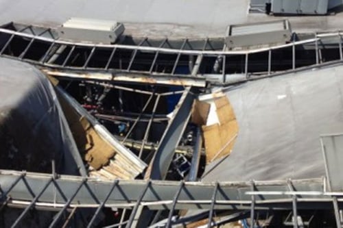 Schade aan een gebouwenstructuur, met een groot gat in het dak en blootgestelde metalen balken.