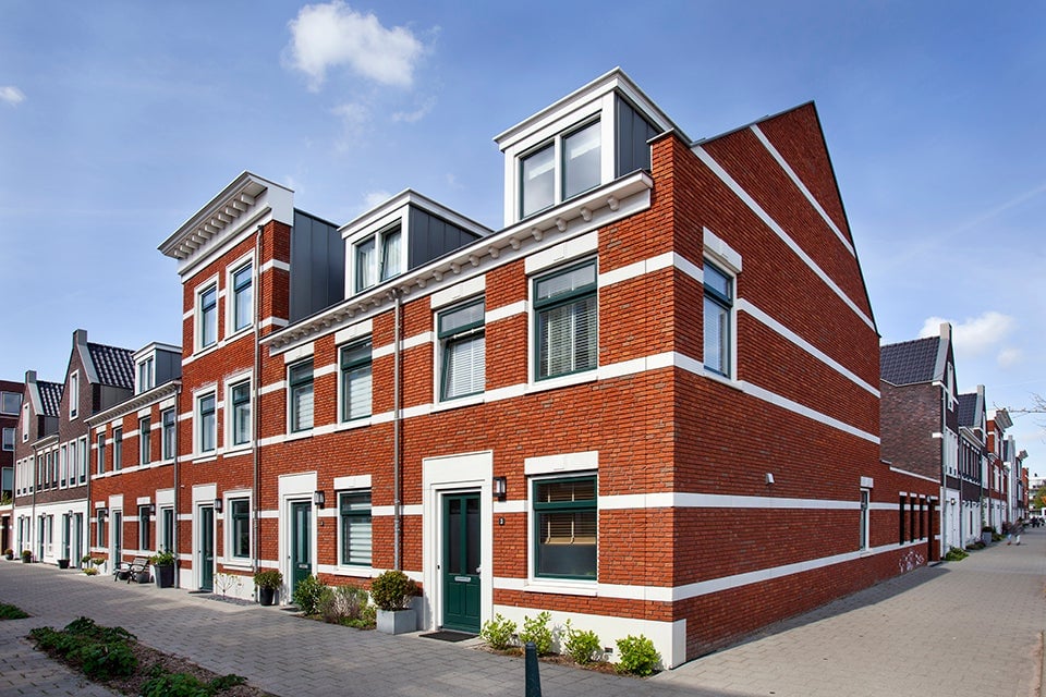 Rij van moderne bakstenen huizen met witte accenten en groene deuren, gelegen aan een rustige straat onder een blauwe lucht.