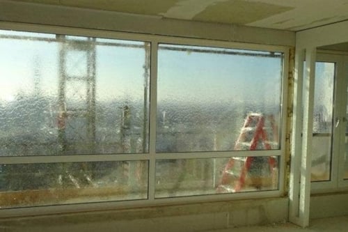 Uitzicht vanuit een gebouw met grote ramen, een vervaagde bouwkraan en een rode ladder zichtbaar buiten.