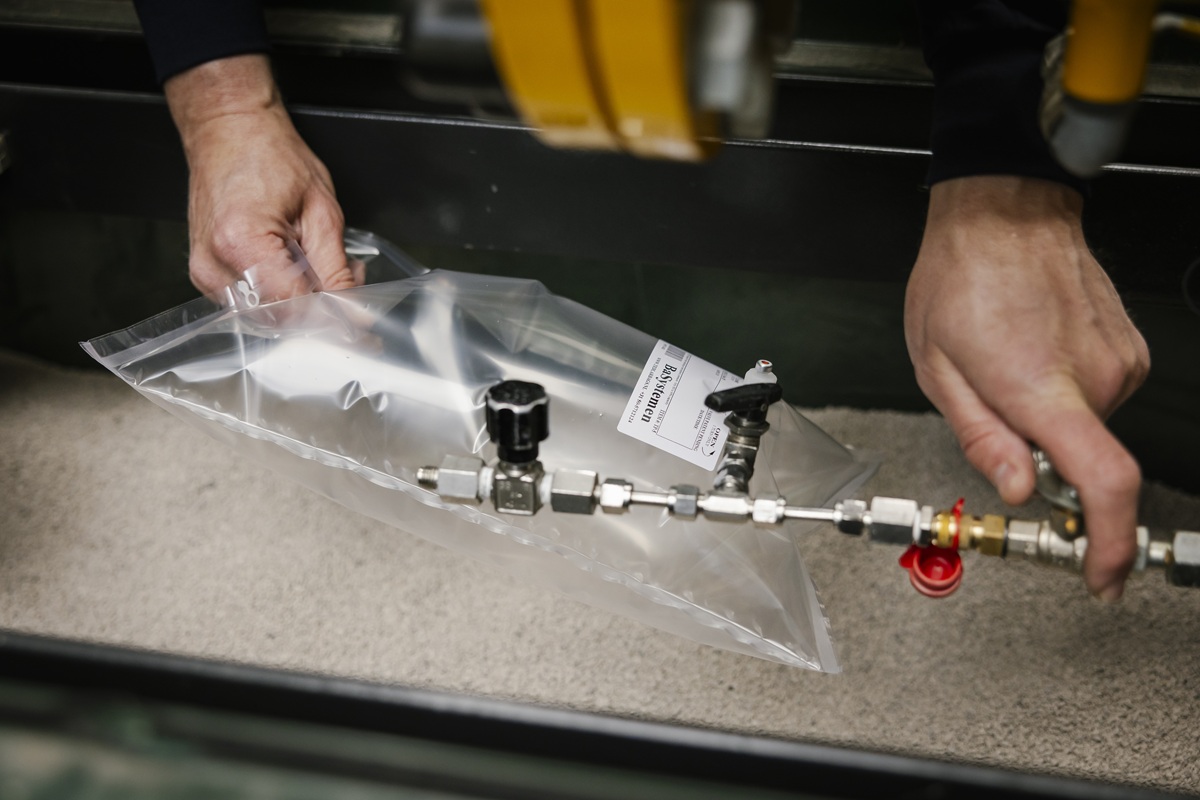 Handen die een transparante zak met een buis en metalen connectoren vasthouden in een technische omgeving.