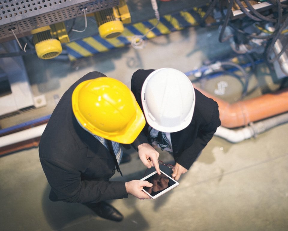 Två inspektörer, med varsin bygghjälm i olika färger, sedda ovanifrån