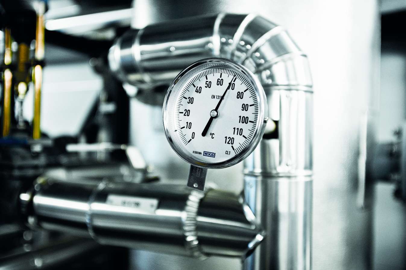 Ett närbildsfoto av en tryckmätare monterad på ett rörsystem i en industriell miljö.