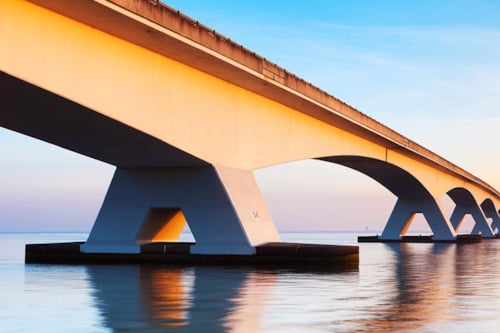 En lång modern bro av betong, över lugnt och stilla vatten.