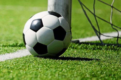 Fotboll på gräsplan nära mål med nät.