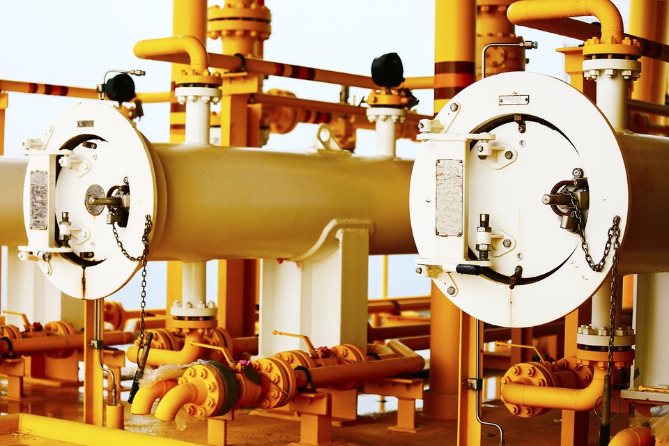 Gula rör och ventiler i en industriell anläggning, med stora vita flänsar och metallkedjor.