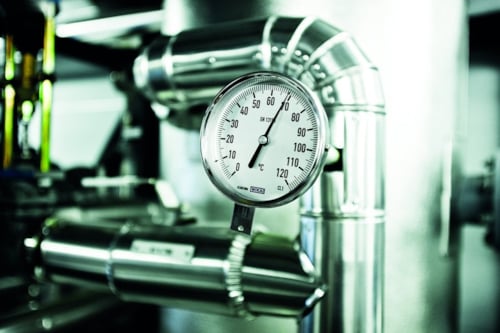 Manometer som mäter tryck, omgiven av metallrör i en industriell miljö.