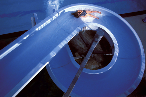 En person åker i en lång blå vattenrutschbana som skruvar sig nästan 360 grader.