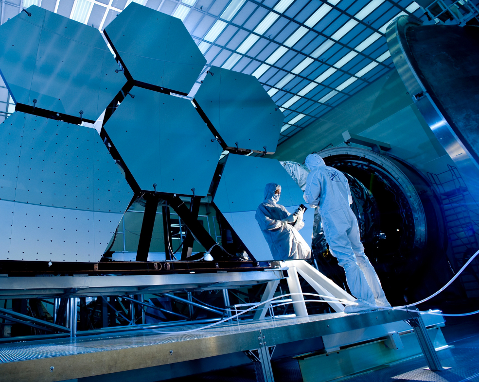 Scientists in clean suits working on large hexagonal mirrors in a laboratory, highlighting advanced technology and precision engineering