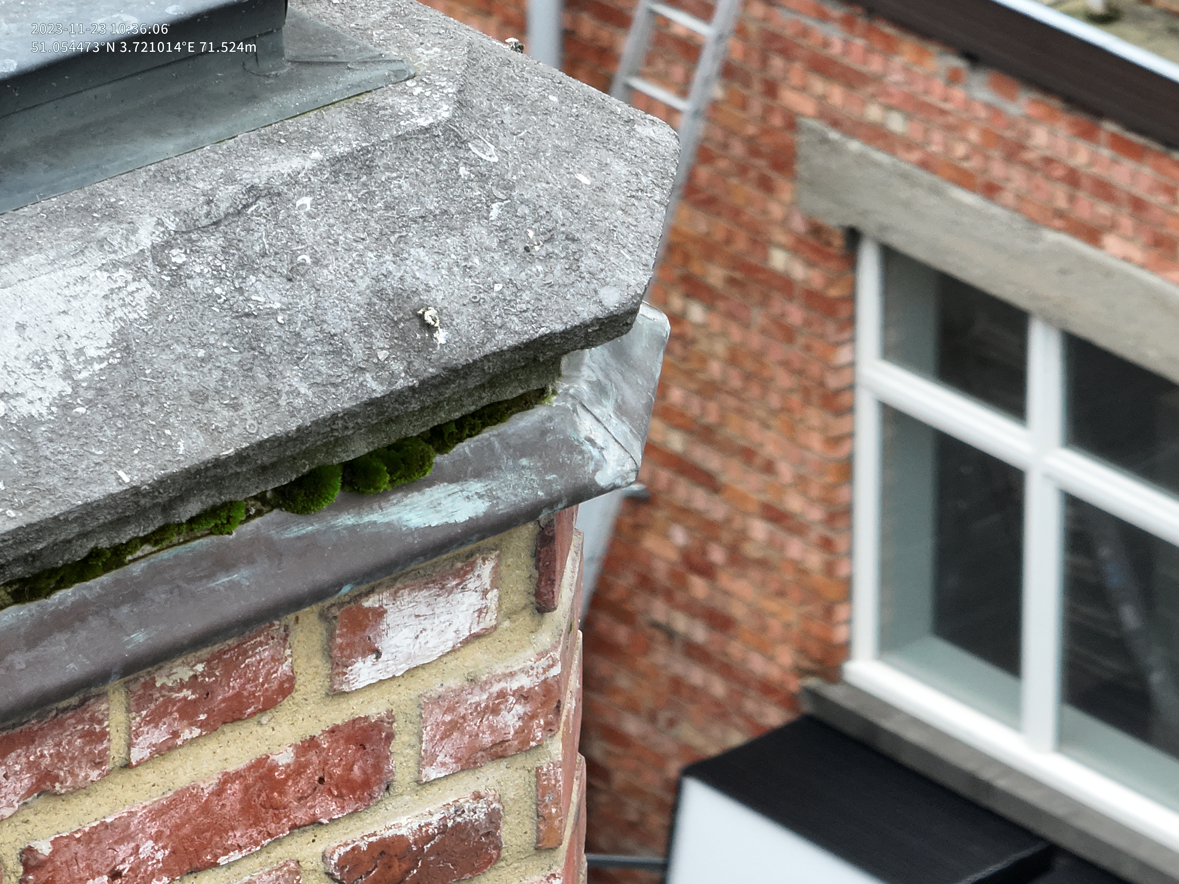 Footage of an old brick chimney with moss growth from a facade inspection, showing building exterior and window in the background, captured from a high angle