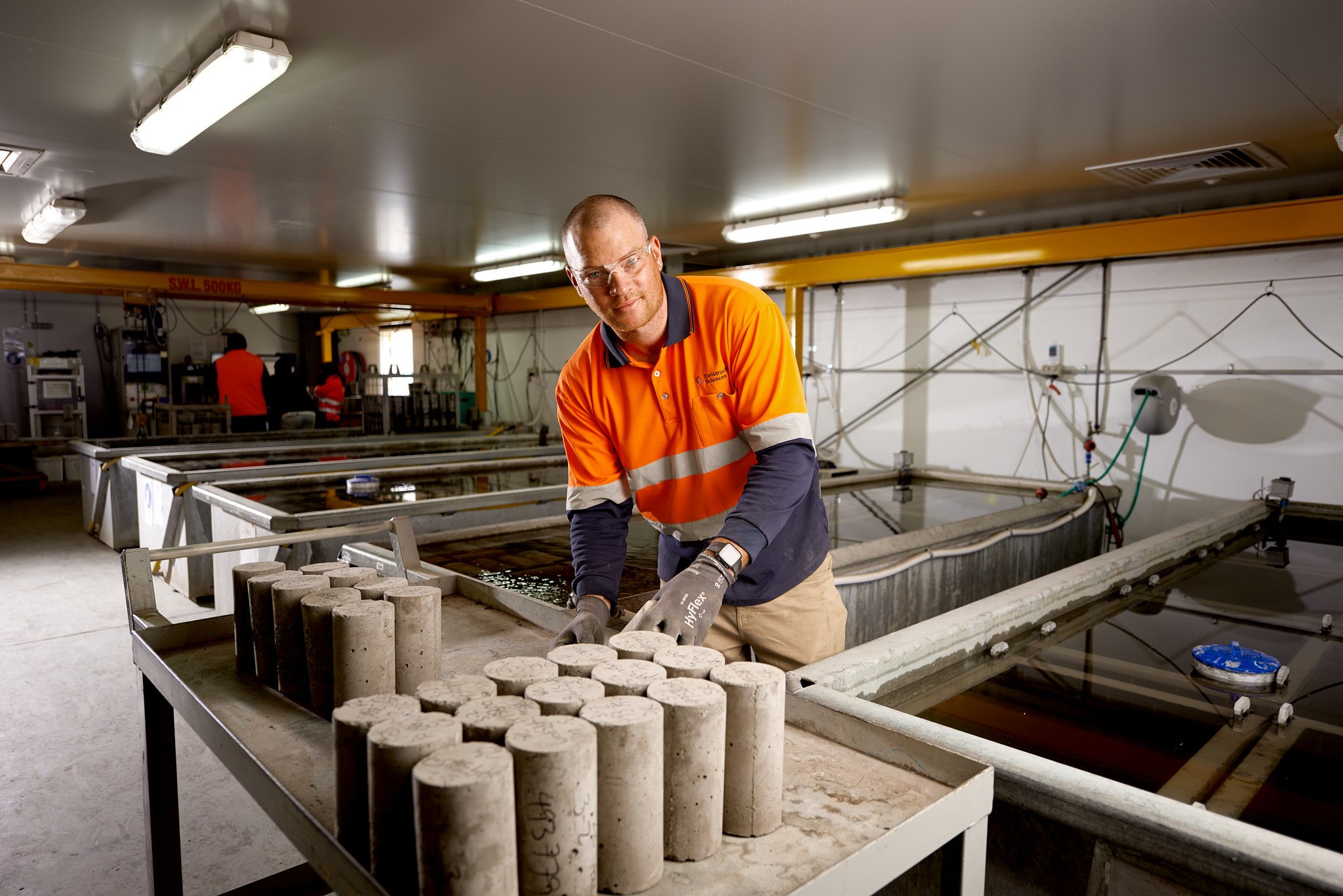 Kiwa laboratory employee in safety gear handling concrete cylinders in a testing laboratory.