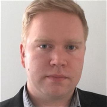 Portrait of a man with blond hair, wearing a dark suit jacket and light-colored shirt, facing forward against a neutral background