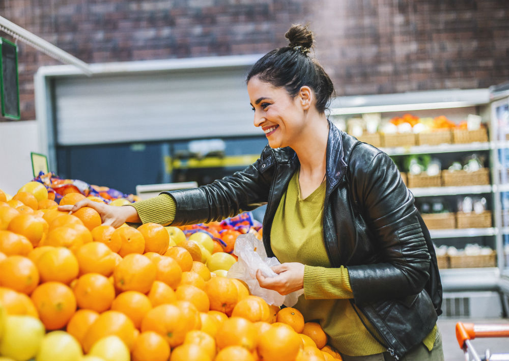 Woman choosing Kiwa organic certified oranges at a grocery store produce section