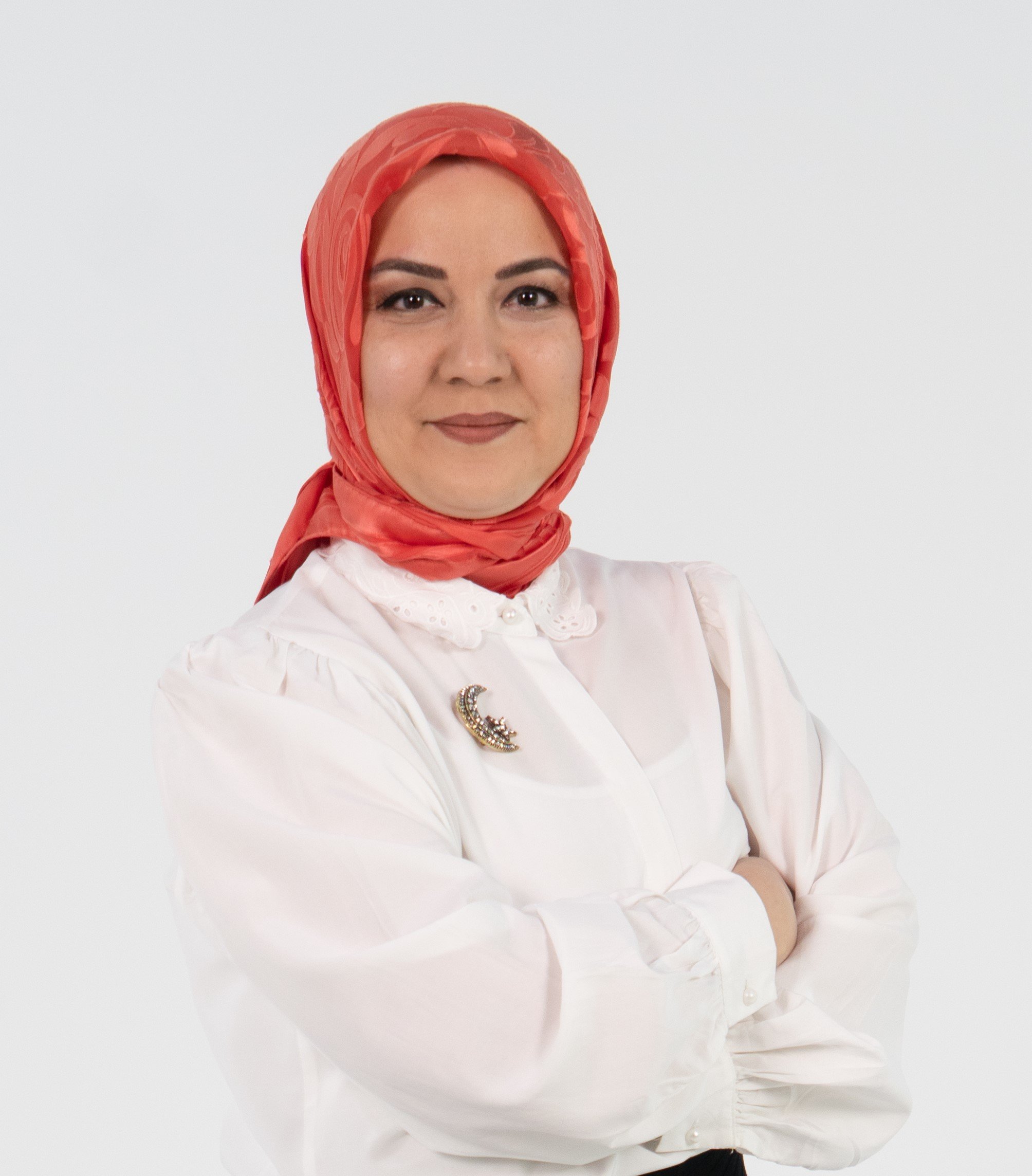 Woman wearing a red headscarf and white blouse with a brooch, arms crossed, smiling confidently against a white background