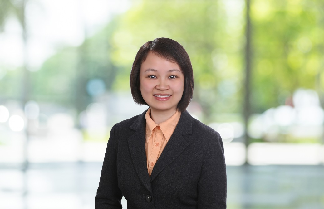 Professional woman in a business suit smiling in front of a blurred green outdoor background