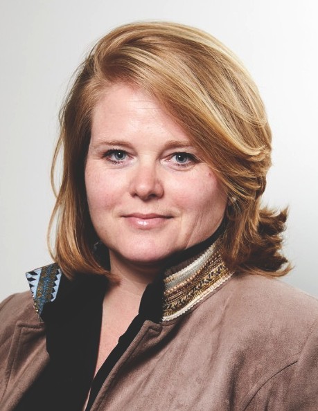 Marjolein Veenstra, Kiwa employee, with shoulder-length red hair wearing a brown jacket and patterned collar, posing against a neutral background
