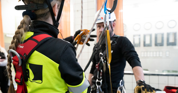 Personer utrustade med säkerhetssele och hjälm under en klättringsövning inomhus.
