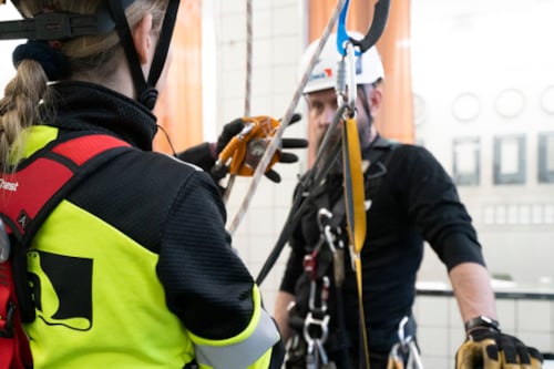 Personer utrustade med säkerhetssele och hjälm under en klättringsövning inomhus.