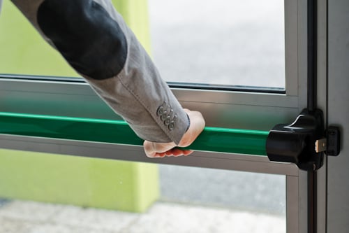 Hand opent een nooddeur met een groene panieksluiting.