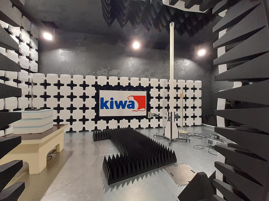 Anechoic chamber interior with Kiwa logo, featuring soundproof walls, acoustic foam spikes, and testing equipment