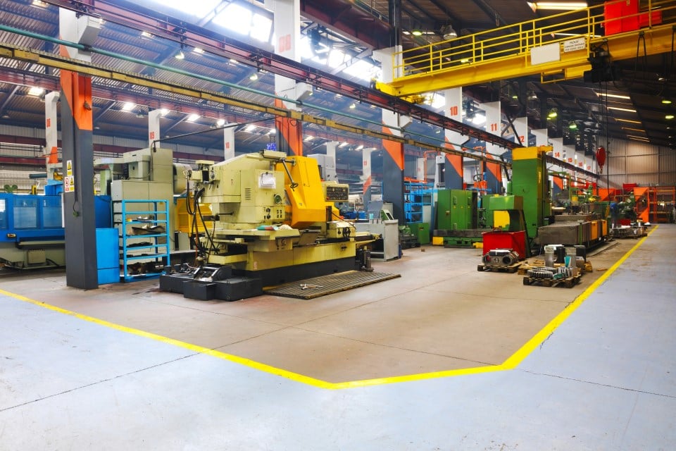 A spacious industrial workshop filled with various machines and equipment, featuring bright lighting and organized work areas.