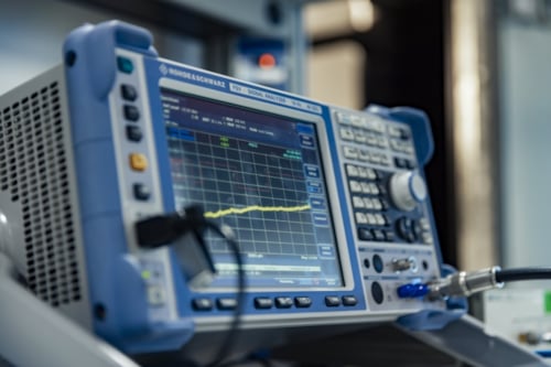 Signal analyzer device displaying a frequency waveform on screen in a laboratory setting