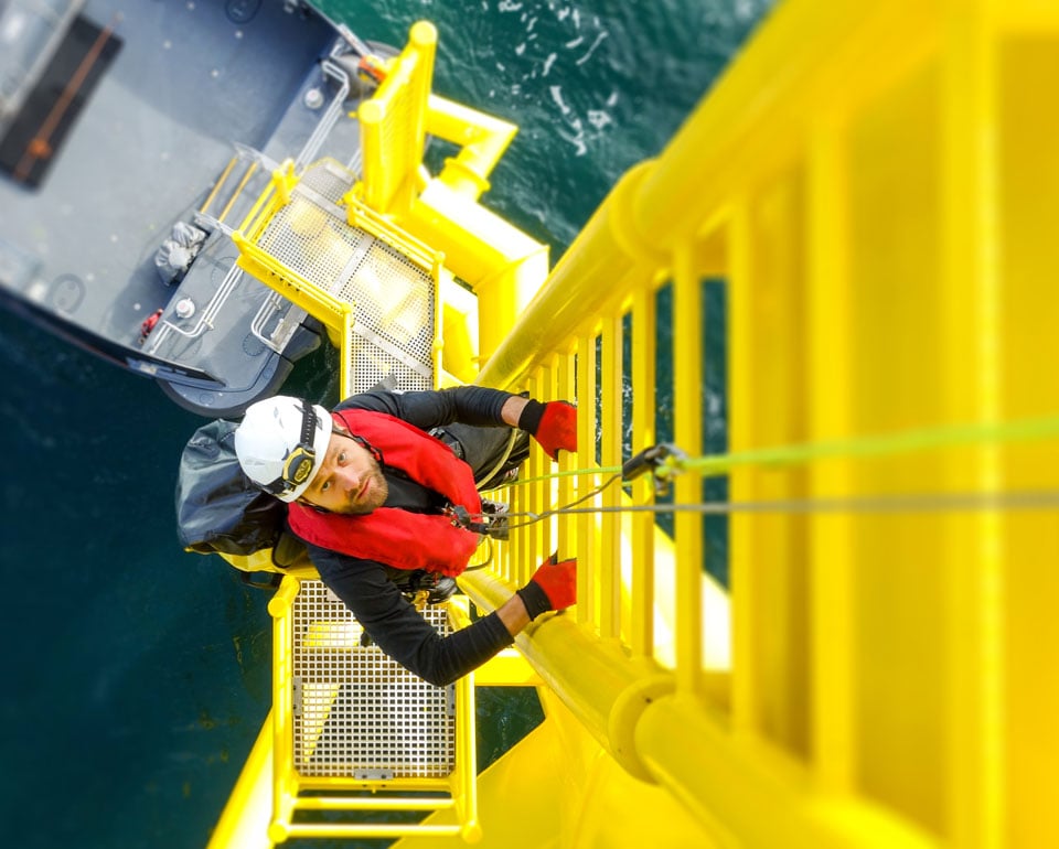 man climbing the stairs to the top of a floating windmill in the sea